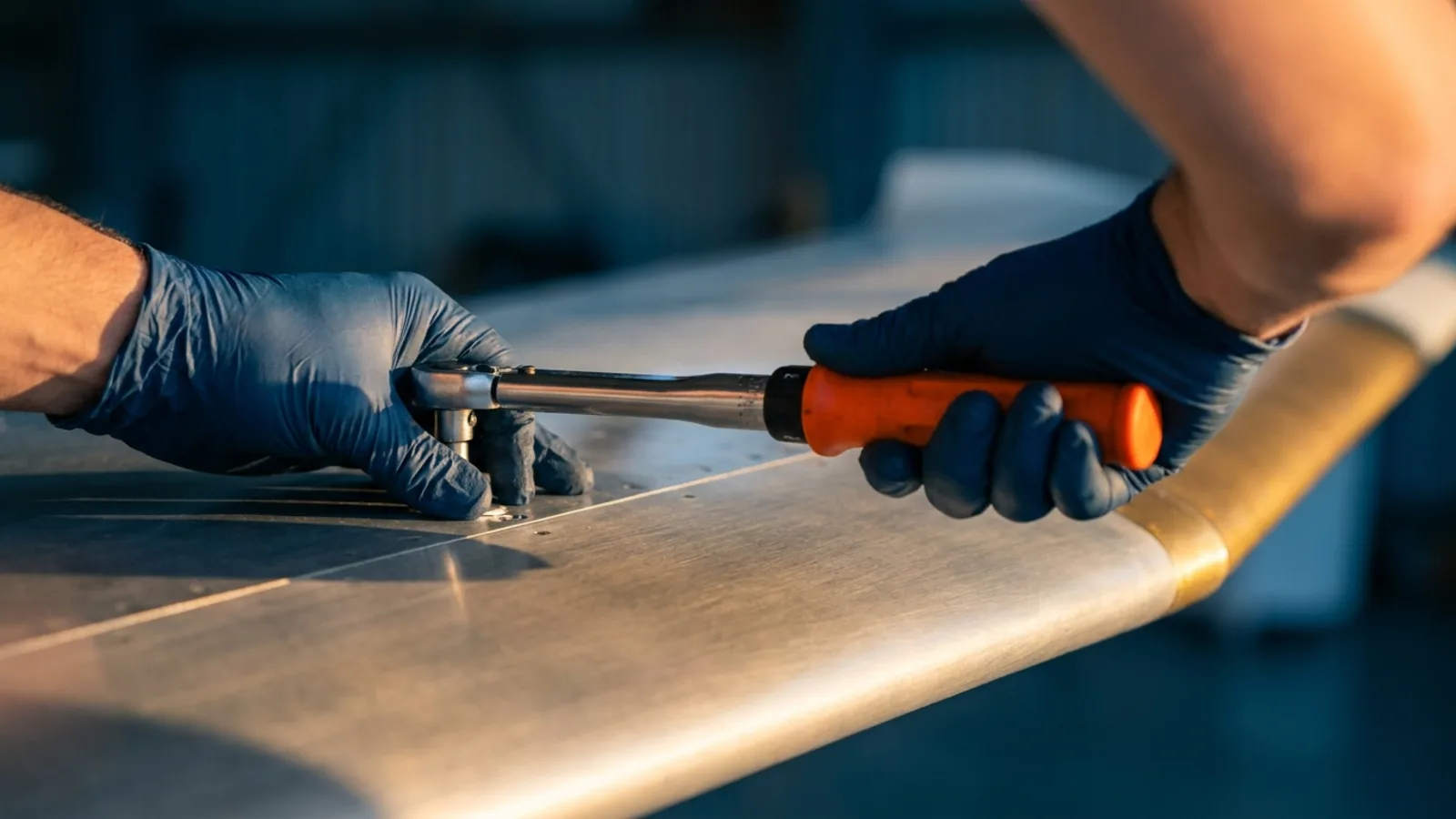 Close-up of a mechanic's gloved hands torquing a fastener on an aircraft wing panel with a torque wrench